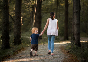 Brother and sister holding hands walking down path through forest