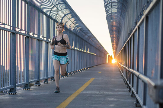 Young tattooed woman running on bridge with sunset behind