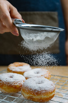 Cropped hand of woman sifting icing sugar on fried donuts