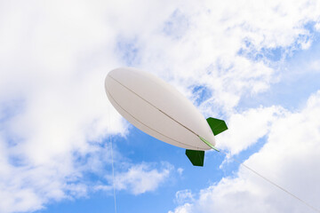 White inflatable airship dirigible zeppelin with green wings in blue sky