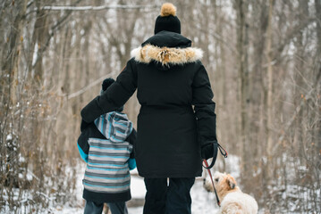 Mother and son walking dog on snowy trail through the woods.