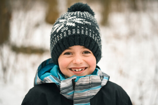 Close up of smiling young boy outside in winter wearing clothing.