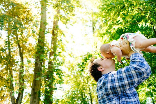 Side view of a man kissing his daughter while lifting her in the air