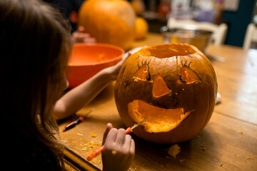 Young girl carving a pumpkin at table with family