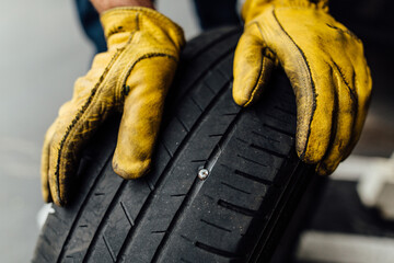 Dirty yellow leather mechanic gloves holding car tire with nail in it