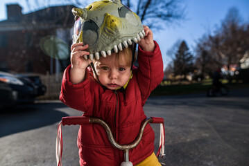 young boy wearing jacket outside on tricycle pulling helmet off head