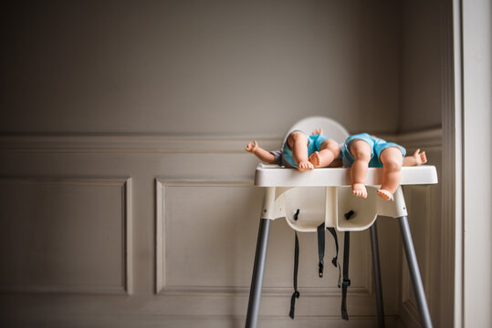 two baby dolls laying on high chair tray with legs dangling over edge