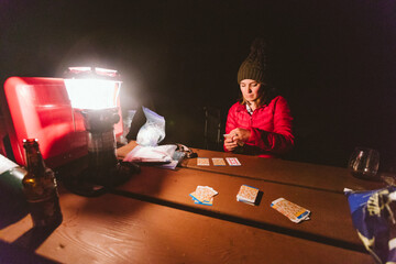 Young woman playing card game in the evening at her campsite