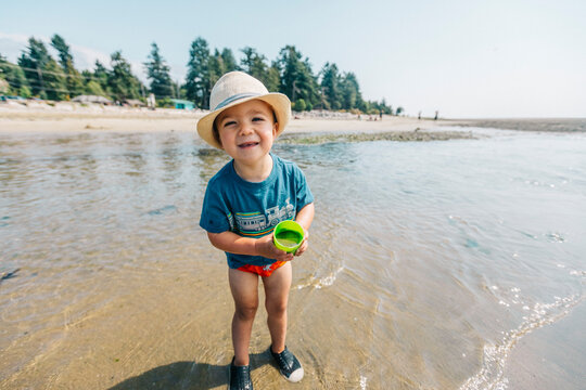 Toddler boy holding small bucket on sandy beach