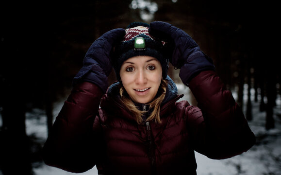 Woman Smiling With Head Torch On And Winter Gear In The Forest Snow