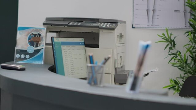 Hospital reception counter with computer and printer to help with medical appointments and healthcare insurance support. Empty registration desk in lobby to fill in checkup reports and forms.