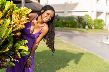 Black woman with long natural hair smiling happily peeking out from behind a croton plant © Oren Thomas