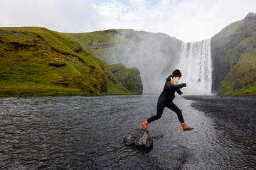 A millenial woman jumps from a rock near Skogafoss, Iceland.
