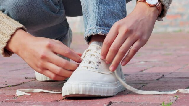 Hands tying sneakers shoes laces on feet in city street, casual fashion and urban road style outdoors. Trendy walking woman, prepare footwear ready and comfortable fitting strings on cool sidewalk