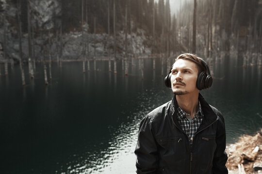 Young man wearing headphones and listening music at the mountain lake
