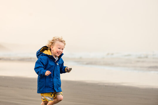 Happy young boy holding a shell running on a beach at dusk