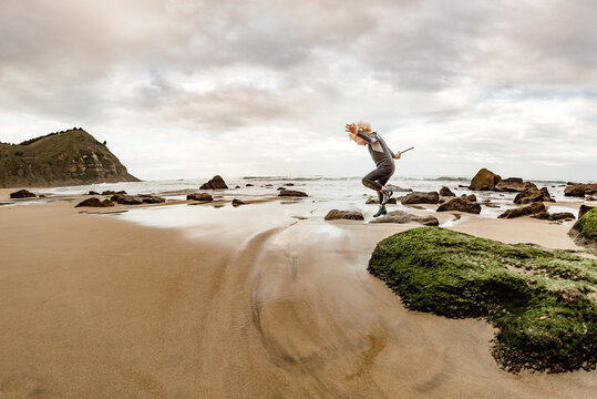 Young boy holding stick jumping from green rock at a beach