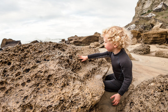 Blonde curly haired boy examining rock at beach