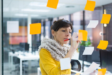 Businesswoman writing on window in creative office seen through glass