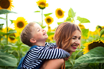 Woman standing in the sunflower field, holding her son on her back.