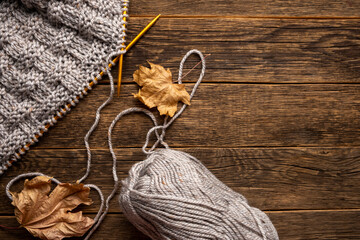 Wool and knitting, knitting needles and dry leaves on wooden background. Autumn season.