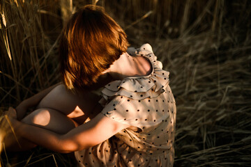 Back view of the woman in dress sitting in a wheat field at sunset