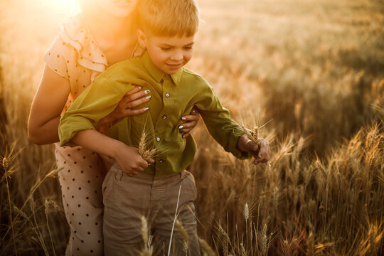 A mother and son playing together in the wheat fields during sunset