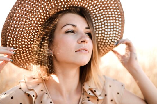 Beautiful young woman in a straw hat and dress in a field at sunset