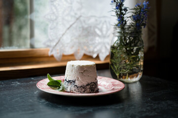 Side view of homemade goat cheese on plate with herbs by window