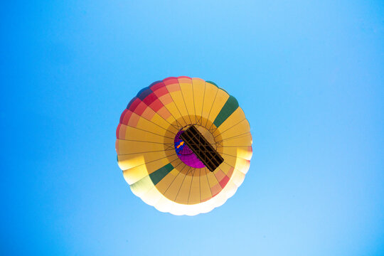 An inflated hot air balloon ascends into a clear blue sky