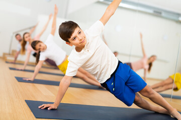 Fototapeta na wymiar Teen boy exercising with sister, mother and father at yoga class, friendly family practicing self-care