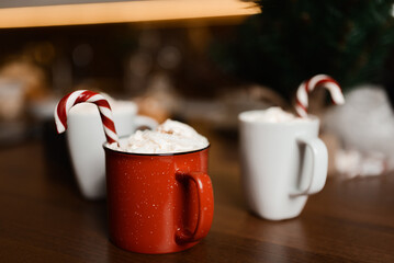 Hot drink with marshmallows and candy cane in red mug. Fir cones, spices in the background. Cozy...