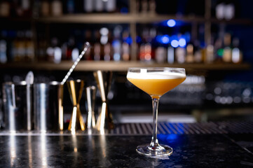 glass with yellow lemon cocktail on the bar; on a black background. the drinks is decorated with lemon zest