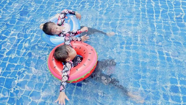 Asian two children little girls and boy playing in outdoor swimming pool on inflatable toy ring, Happy brother and sister playing in the pool tropical resort during family summer vacation