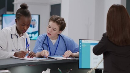 Diverse medical team working at hospital reception desk ith receptionist, analyzing checkup papers to help with healthcare appointments. Specialists writing insurance report at registration counter.