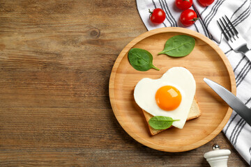 Tasty fried egg in shape of heart with toast served on wooden table, flat lay. Space for text