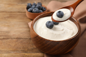 Eating tasty yogurt with blueberries from bowl on wooden table, space for text