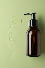 Bottle and drops of hydrophilic oil on light green background, flat lay