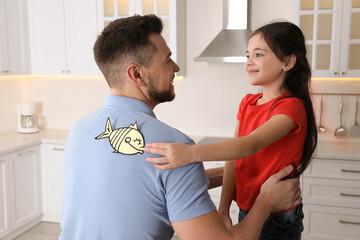 Cute little girl sticking paper fish to father's back at home