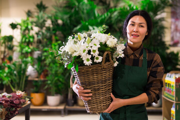 Fototapeta premium Portrait of a confident and successful Asian florist woman standing in a shop with flowers in her hands