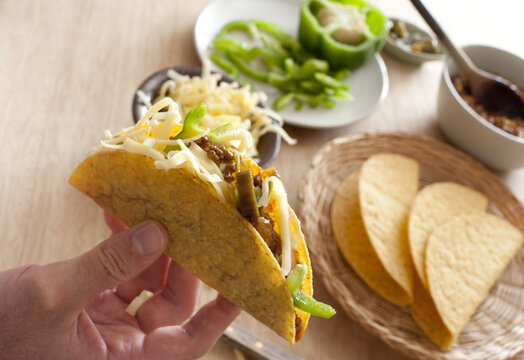 Man Preparing A Ground Beef Taco Adding Fresh Green Peppers And Grated Cheese For A Tasty Lunchtime Snack