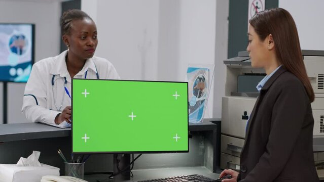 Diverse medical team using computer with greenscreen at reception counter. Facility staff working with isolated copyspace background, blank mockup template and chroma key display on monitor.