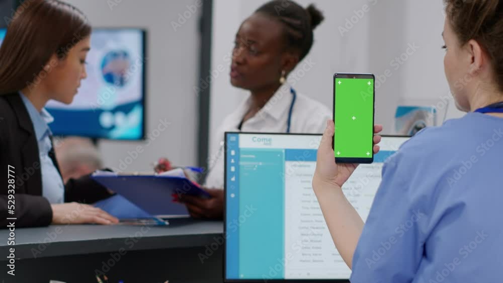 Wall mural medical assistant holding smartphone with greenscreen display at hospital reception counter. nurse u
