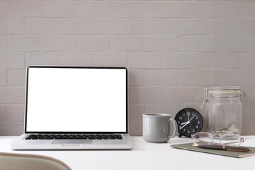 Laptop with white empty display. coffee cup and notebook on white table.