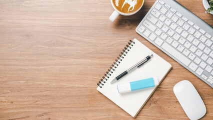 Office wooden desk with keyboard, notebook, pen, mouse and cup of coffee, Top view wth copy space, Flat lay.