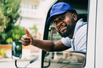 Portrait of courier black man in the truck thumb up and smiling to camera while sitting in driver...