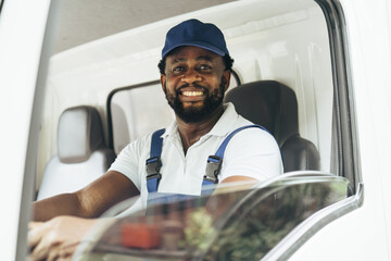 Portrait of courier black man in the truck thumb up and smiling to camera while sitting in driver seat, Optimistic man worker with delivery occupation.