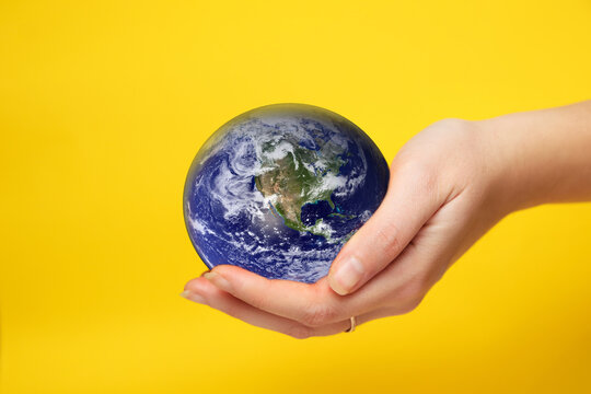 Defocus female hand holding planet globe on yellow background. Environmental protection concept. Earth in hands. Save of Earth. Elements of this image furnished by NASA. Out of focus