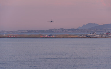 Last airplane lands over the Mediterranean sea to Nice airport at sunset during the busy vacation...