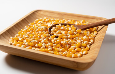 Dried corn kernels in wooden bowl placed on white background.